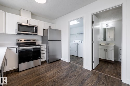 Modern kitchen featuring white cabinetry, stainless steel appliances, and wood-finish flooring - #136, 180 Bridgeport Bv, Leduc, AB - Indoor Photo Showing Kitchen