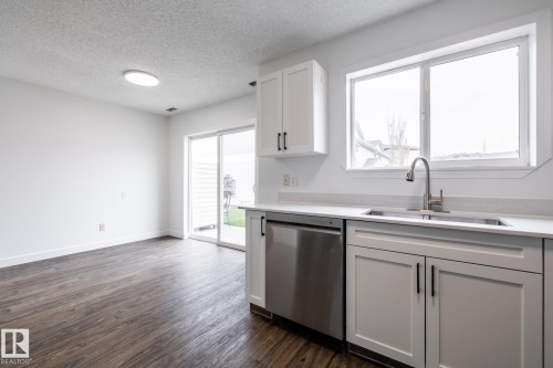 Kitchen area featuring white shaker-style cabinetry with matte black hardware, a stainless steel sink with a gooseneck faucet, and a stainless steel dishwasher - #136, 180 Bridgeport Bv, Leduc, AB - Indoor Photo Showing Kitchen With Double Sink
