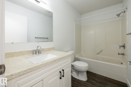Bright bathroom featuring a white vanity with an integrated sink, a speckled light countertop, and brushed nickel fixtures - #136, 180 Bridgeport Bv, Leduc, AB - Indoor Photo Showing Bathroom