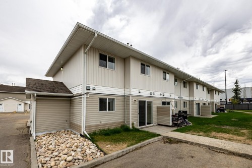 Multi-story exterior featuring light beige siding, individual patios with concrete surfaces, multiple windows, and a sloped roofline - #136, 180 Bridgeport Bv, Leduc, AB - Outdoor