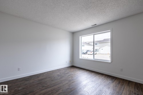 Spacious room featuring wood-finish flooring, white baseboards, and a large window - #136, 180 Bridgeport Bv, Leduc, AB - Indoor Photo Showing Other Room
