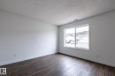 Spacious room featuring wood-finish flooring, white baseboards, and a large window - #136, 180 Bridgeport Bv, Leduc, AB  - Indoor Photo Showing Other Room 