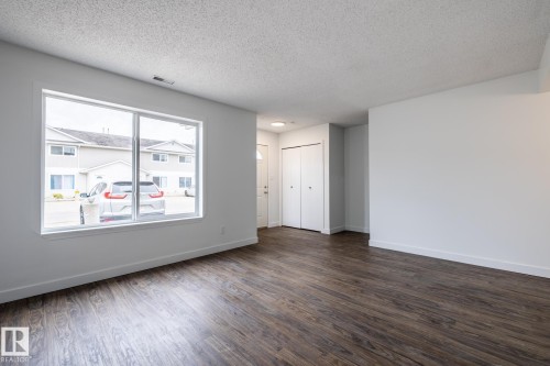 Spacious living area featuring wood-finish flooring, a large window, and white trim - #136, 180 Bridgeport Bv, Leduc, AB - Indoor Photo Showing Other Room