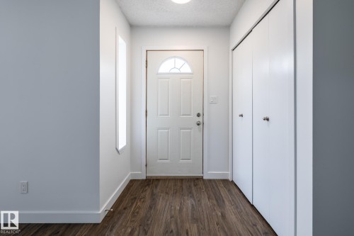 Entryway featuring a white paneled door with a half-moon glass insert, wood-finish flooring, two sets of bi-fold closet doors, and white baseboards - #136, 180 Bridgeport Bv, Leduc, AB - Indoor Photo Showing Other Room