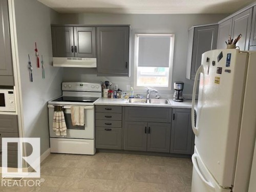 Kitchen featuring gray shaker-style cabinetry, white countertops, and a stainless steel double-basin sink - 5339 52 Ave, Mundare, AB 
