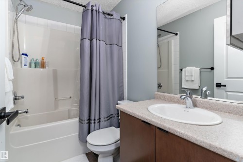 Bathroom featuring a combination shower and tub with white surround, a toilet, and a vanity with an integrated sink and wood-finish cabinetry - 122 3357 16A Avenue, Edmonton, AB - Indoor Photo Showing Bathroom