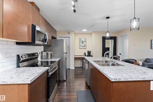 Modern kitchen featuring wood-finish cabinetry, stainless steel appliances, speckled stone countertops, and a subway tile backsplash - 122 3357 16A Avenue, Edmonton, AB - Indoor Photo Showing Kitchen With Double Sink With Upgraded Kitchen