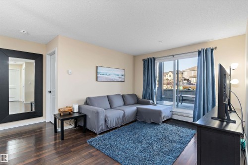 Living area featuring dark wood-finish flooring, light neutral wall paint, and a sliding glass door leading to an outdoor patio - 122 3357 16A Avenue, Edmonton, AB - Indoor Photo Showing Living Room