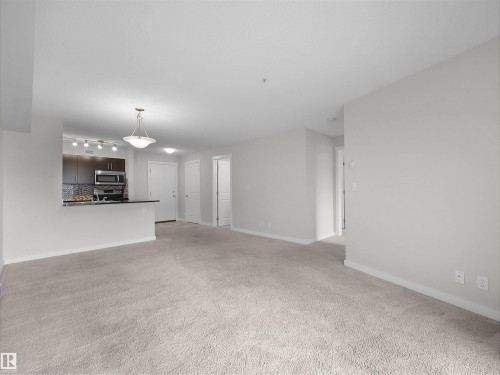 Open-concept living space featuring neutral carpeting and light-toned wall finishes - 220 5804 Mullen Place, Edmonton, AB - Indoor Photo Showing Other Room