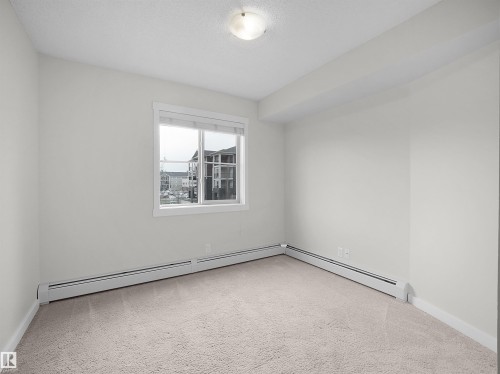 Bright room featuring a window with white trim, light-toned carpeting, white walls, and baseboard heating - 220 5804 Mullen Place, Edmonton, AB - Indoor Photo Showing Other Room