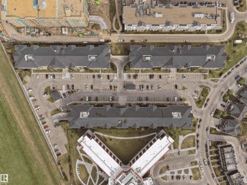 Aerial perspective showcasing multiple buildings with dark-pitched roofs, extensive surface parking areas, and surrounding roadways - 220 5804 Mullen Place, Edmonton, AB - Other