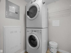 Laundry area featuring stacked front-loading appliances, a wall-mounted wire shelving unit, and tile flooring - 