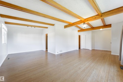 Spacious room featuring exposed wood ceiling beams, light wood-finish flooring, white walls, and a window providing natural light - 6134 37A Avenue, Edmonton, AB 