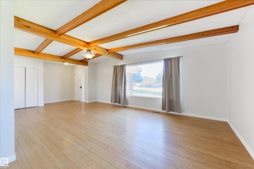 Open living area featuring wood-finish flooring, exposed ceiling beams, and a large window - 6134 37A Avenue, Edmonton, AB 