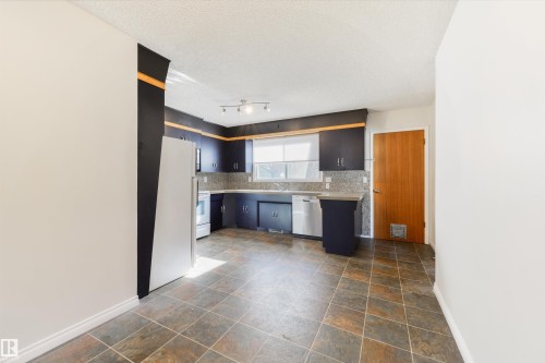 Kitchen featuring dark cabinetry with brushed nickel hardware, stone-finish countertops, and a full-height tile backsplash - 6134 37A Avenue, Edmonton, AB 