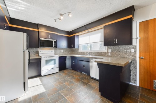 Kitchen featuring dark cabinetry, light-toned countertops, and a full suite of white appliances - 6134 37A Avenue, Edmonton, AB 