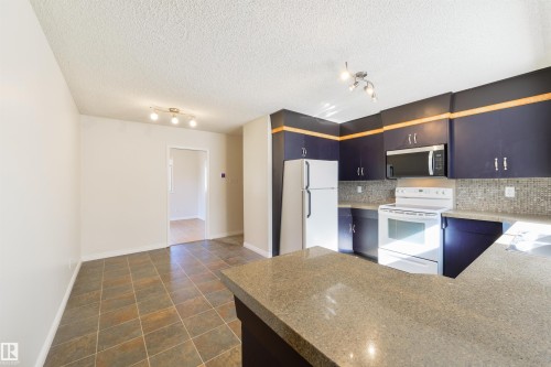Kitchen featuring dark wood cabinetry, a light-colored countertop, and a mosaic tile backsplash - 6134 37A Avenue, Edmonton, AB 