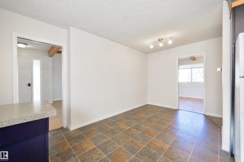 Spacious room featuring multi-toned square tile flooring, track lighting, and white baseboards - 6134 37A Avenue, Edmonton, AB 
