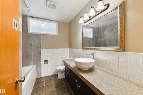 Bathroom featuring a vessel sink, dark wood-finish vanity, light-toned countertop, and framed mirror with integrated lighting - 6134 37A Avenue, Edmonton, AB 