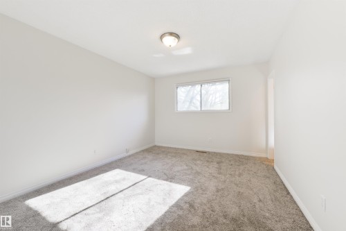 Bright room featuring a window with white trim, gray carpet, white walls, and a ceiling-mounted light fixture - 6134 37A Avenue, Edmonton, AB 