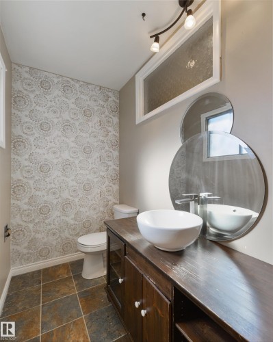 Powder room featuring a vessel sink on a dark wood-finish vanity, patterned accent wall, and multi-toned tile flooring - 6134 37A Avenue, Edmonton, AB 