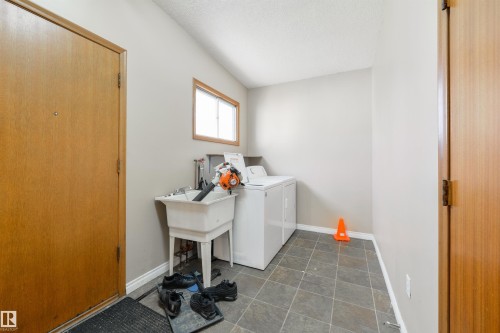 Utility space featuring tile flooring, a window with wood trim, a laundry sink, and a washer - 6134 37A Avenue, Edmonton, AB 
