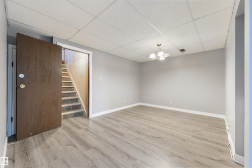 Spacious room featuring light wood-finish flooring, light gray painted walls, and white baseboards - 6134 37A Avenue, Edmonton, AB 