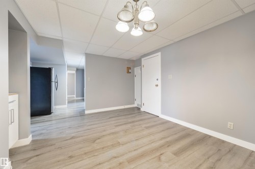 Open-concept area featuring light wood-finish flooring, a neutral color palette, white baseboards, a white ceiling with recessed panels, and a multi-bulb ceiling fixture - 6134 37A Avenue, Edmonton, AB 