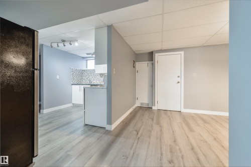 Spacious room featuring wood-finish flooring, light grey painted walls, white baseboards, and a drop ceiling - 6134 37A Avenue, Edmonton, AB 