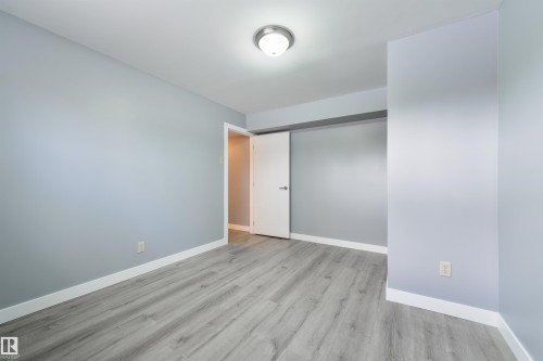 Spacious room featuring wood-finish flooring, light blue walls, white baseboards, and a flush mount ceiling light - 6134 37A Avenue, Edmonton, AB 