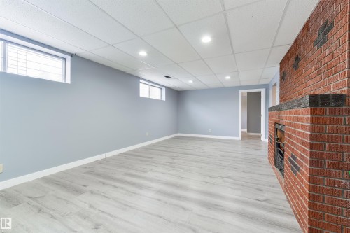 Spacious interior featuring a brick fireplace, light wood-finish flooring, recessed lighting, and pale blue wall tones - 6134 37A Avenue, Edmonton, AB 