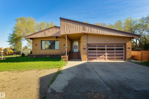 Brick exterior featuring an integrated garage with a panel door, concrete driveway, and covered front entry - 6134 37A Avenue, Edmonton, AB 