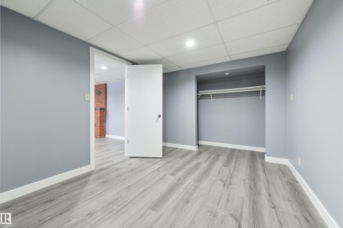 Spacious room featuring light grey wood-finish flooring, crisp white baseboards, and neutral grey wall paint - 6134 37A Avenue, Edmonton, AB 