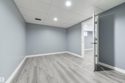 Spacious room featuring wood-finish flooring, light blue walls, crisp white baseboards, and a white drop ceiling with recessed lighting - 6134 37A Avenue, Edmonton, AB 