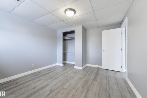 Spacious room featuring light gray walls, wood-finish flooring, white trim, a built-in closet with shelving and hanging rod, and a flush-mount ceiling light - 6134 37A Avenue, Edmonton, AB 