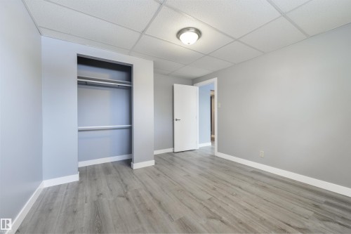 Spacious room featuring light wood-finish flooring, a neutral wall color, and a built-in closet with shelving and hanging rods - 6134 37A Avenue, Edmonton, AB 