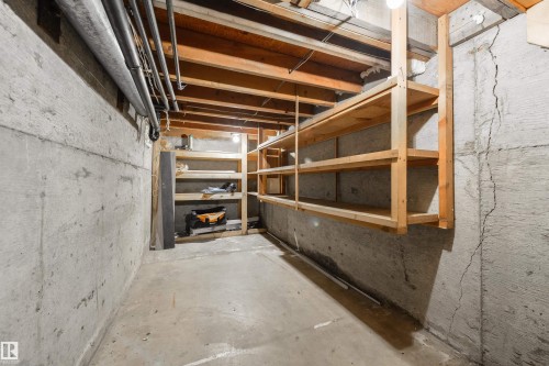 Concrete basement featuring exposed wooden joists, ceiling-mounted utilities, concrete flooring, and built-in wooden shelving units - 6134 37A Avenue, Edmonton, AB 