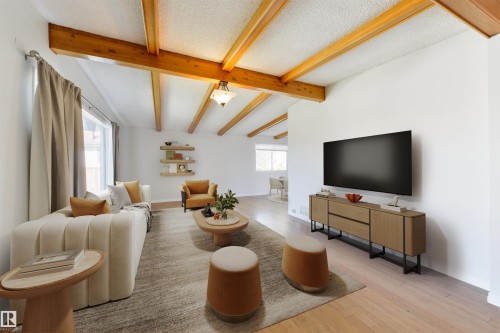Spacious living area featuring exposed wood ceiling beams, wood-finish flooring, and a large window with natural light - 6134 37A Avenue, Edmonton, AB 