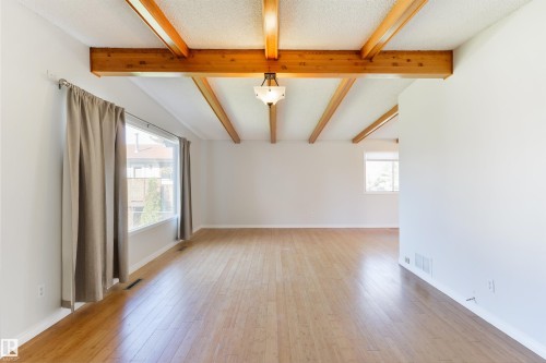 Spacious interior featuring exposed wood beams, wood-finish flooring, white painted walls, and a large window with natural light - 6134 37A Avenue, Edmonton, AB 