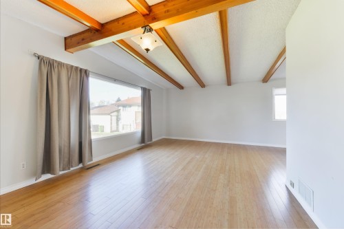 Spacious interior featuring exposed wood beams, wood-finish flooring, a large picture window, and recessed lighting - 6134 37A Avenue, Edmonton, AB 