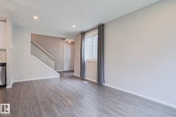 Spacious interior featuring wood-finish flooring, recessed ceiling lighting, a staircase with a wooden handrail, a kitchen backsplash with subway tiles, and a window with blinds - 