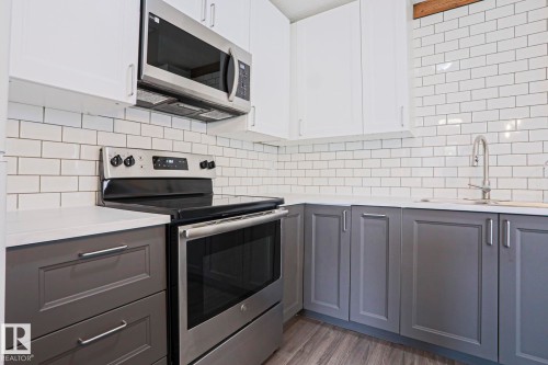 Modern kitchen featuring stainless steel appliances, white subway tile backsplash, white upper cabinetry, and contrasting gray lower cabinetry with contemporary hardware - 35 Chungo Drive, Devon, AB - Indoor Photo Showing Kitchen With Double Sink With Upgraded Kitchen