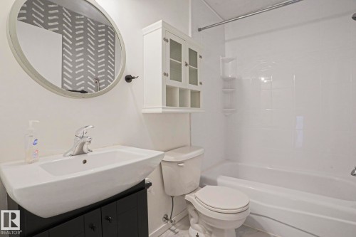 Bathroom featuring a white vanity sink, chrome faucet, black vanity base, an oval mirror, and a white bathtub with white tiled surround - 35 Chungo Drive, Devon, AB - Indoor Photo Showing Bathroom