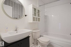 Bathroom featuring a white vanity sink, chrome faucet, black vanity base, an oval mirror, and a white bathtub with white tiled surround - 