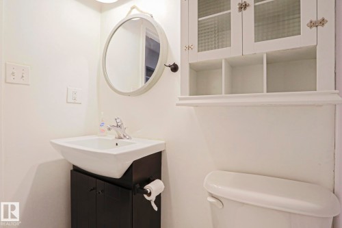 Compact bathroom featuring a white toilet, black vanity with an integrated sink, and a circular wall-mounted mirror - 35 Chungo Drive, Devon, AB - Indoor Photo Showing Bathroom