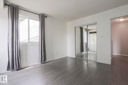 Spacious room featuring wood-finish flooring, two windows, mirrored closet doors, and white walls - 