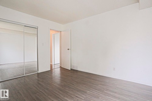 Spacious interior room featuring wood-finish flooring, white walls, and a full-height mirrored closet - 35 Chungo Drive, Devon, AB - Indoor Photo Showing Other Room