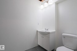 Compact bathroom featuring a white vanity with integrated sink, chrome faucet, and a wall-mounted light fixture with three sconces - 