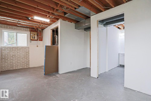 Unfinished basement space featuring exposed ceiling joists, concrete flooring, perimeter brick-textured wall paneling, and a window for natural light - 35 Chungo Drive, Devon, AB - Indoor Photo Showing Basement