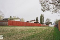 Expansive grassy lot with a long, red-stained privacy fence bordering the property - 